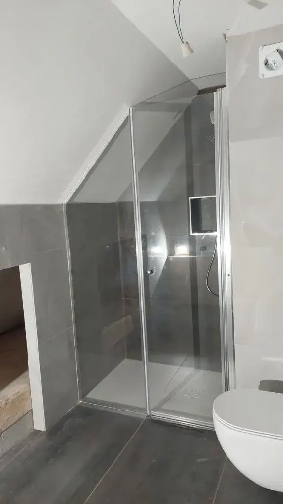 Tuš kabina po meri v vogalu mansarde — kaljeno steklo 8 mm, krom okovje in profili. Prilagojeno poševnemu stropu. Družinska h
